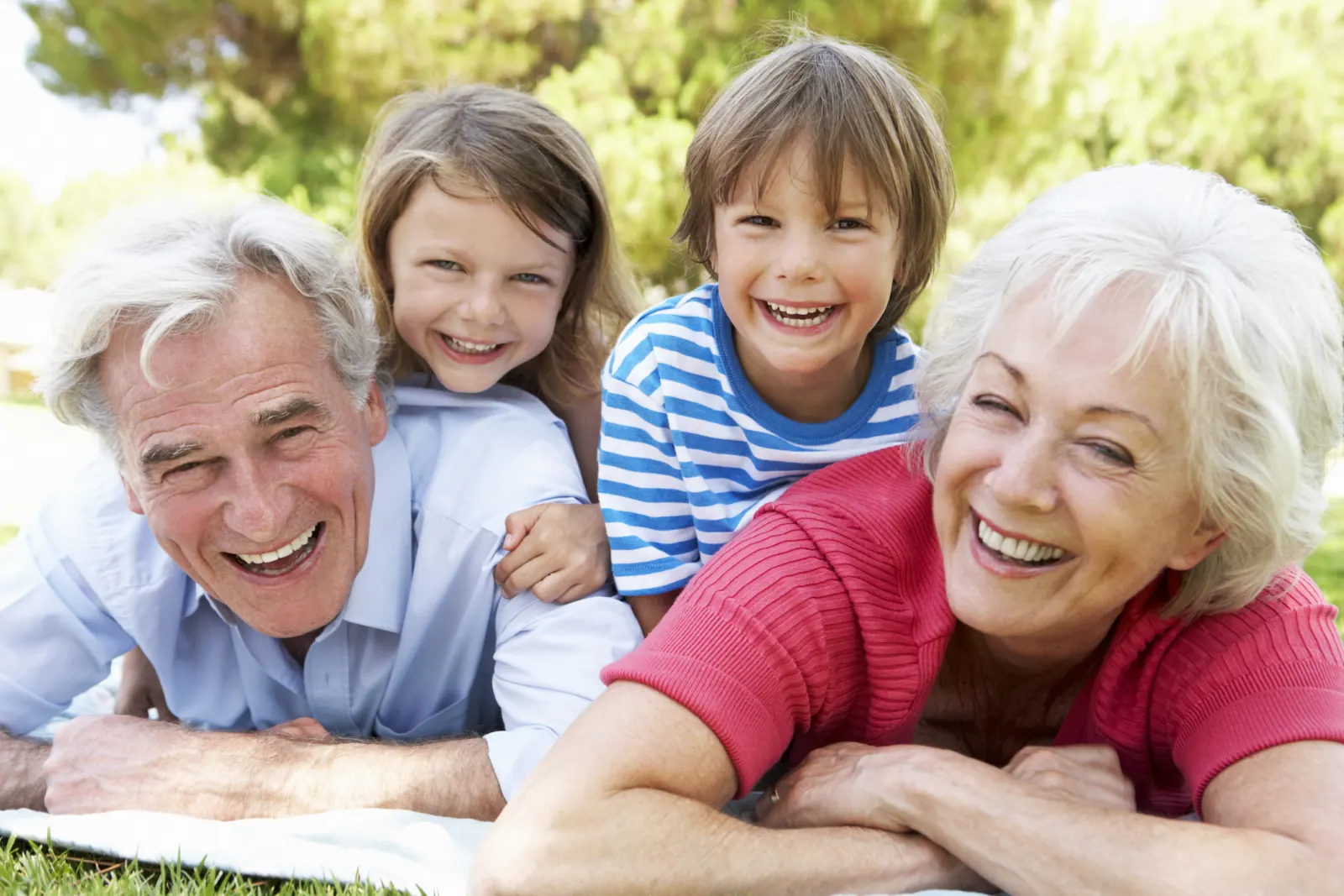 Smiling grandparents lying on the grass with their two grandchildren